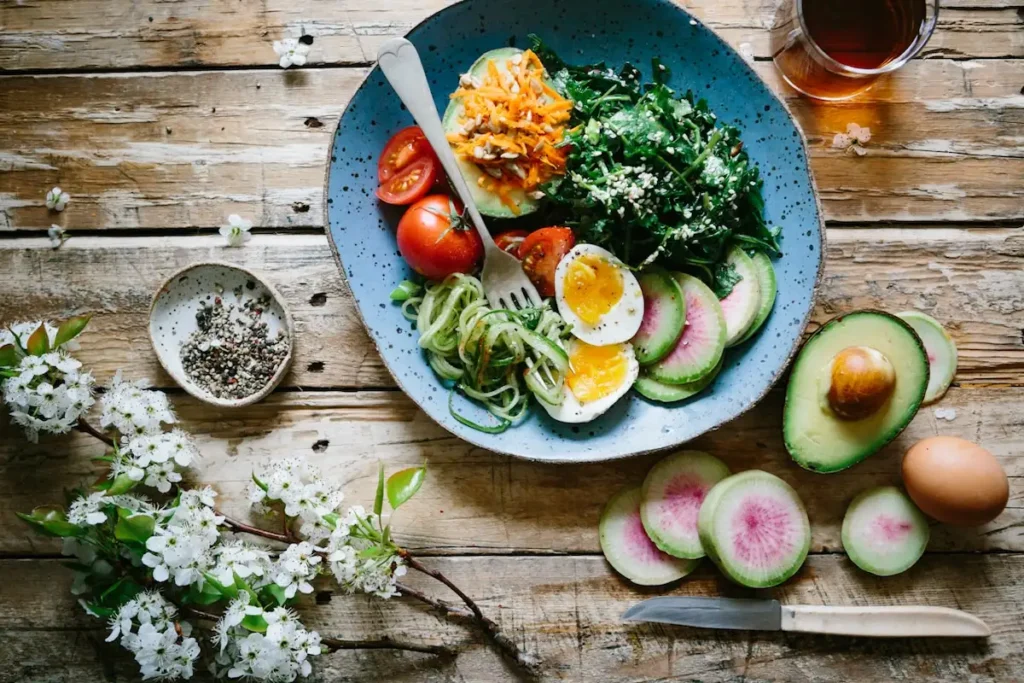 A healthy salad bowl with avocado, eggs, and fresh vegetables on a wooden table.