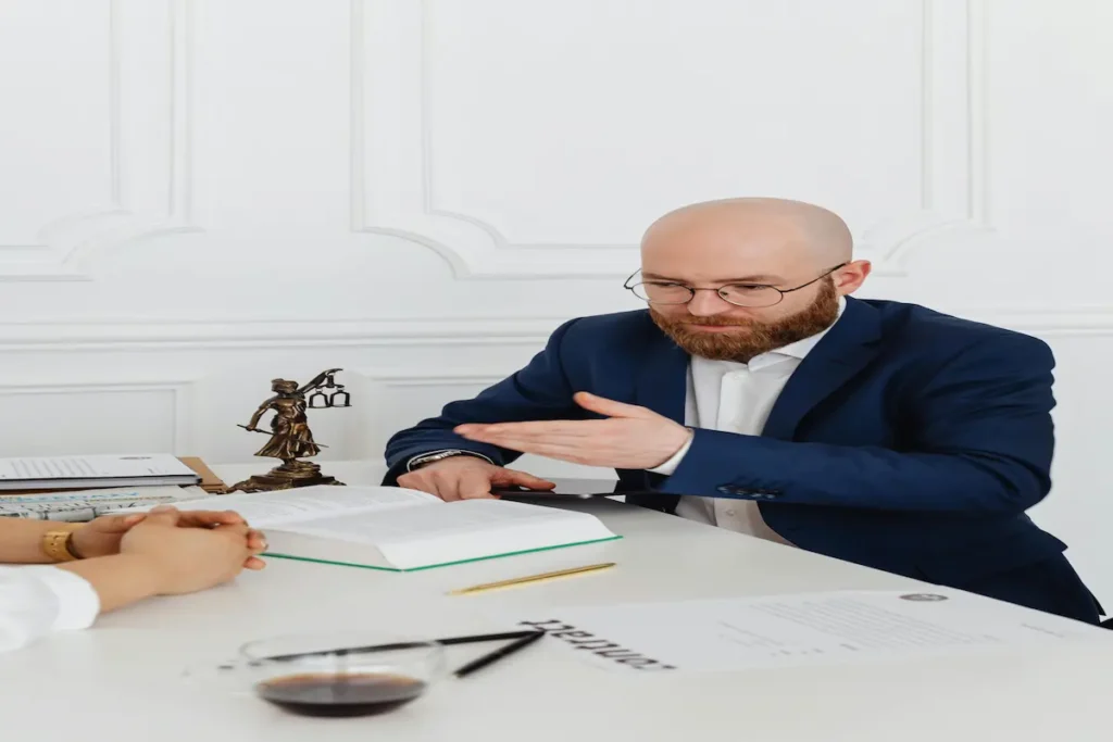 An intellectual property lawyer explaining legal documents and a law book to a client at a desk