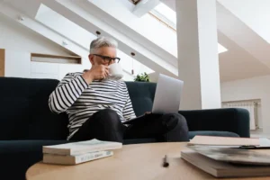 A mature investor relaxing on a sofa with coffee while using a laptop to manage his self directed ira portfolio.