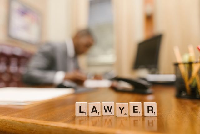 Wooden letter tiles spelling the word LAWYER on an office desk with a professional attorney working in a blurred background.