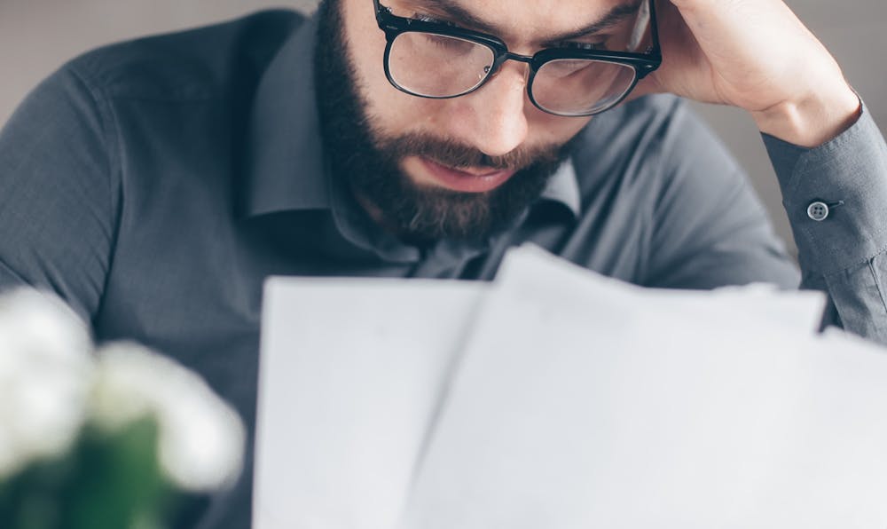 Stressed man in glasses reviewing overwhelming financial documents, illustrating the need for a bankruptcy lawyer to navigate Chapter 7 vs Chapter 13 costs and processes.