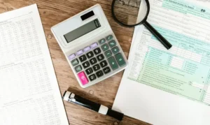 A calculator, magnifying glass, and financial tax forms on a wooden desk, representing detailed research for the best Roth IRA accounts.