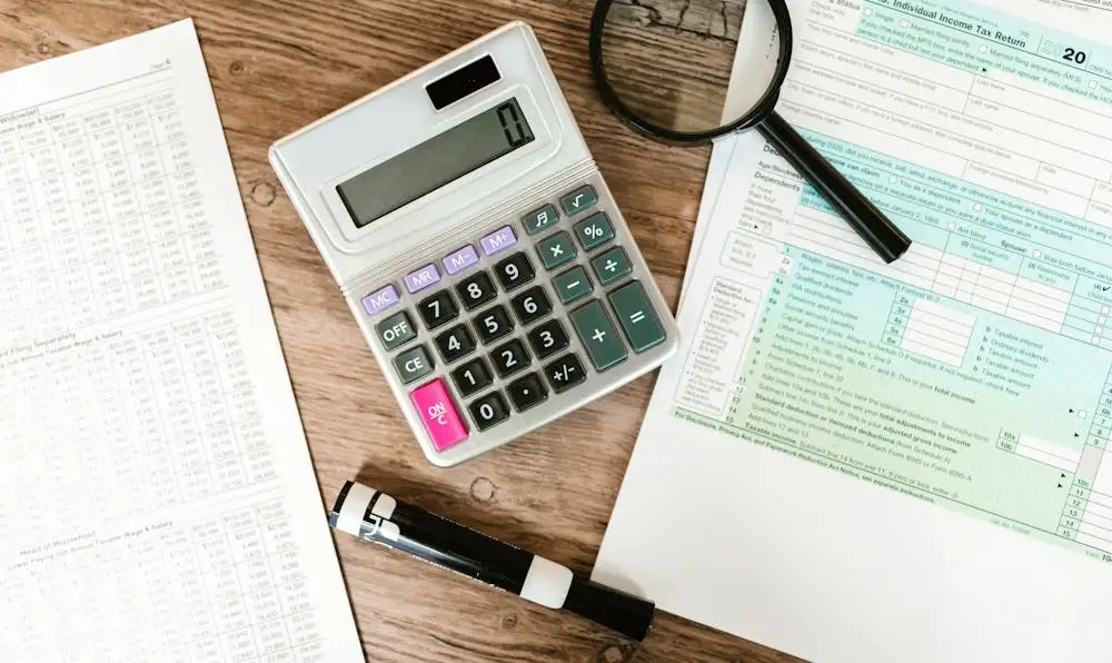 A calculator, magnifying glass, and financial tax forms on a wooden desk, representing detailed research for the best Roth IRA accounts.