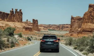 A rental SUV driving on a scenic desert highway in the American Southwest, representing tourists navigating car insurance requirements and costs for foreign drivers in the USA.