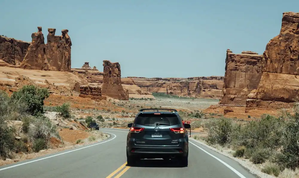 A rental SUV driving on a scenic desert highway in the American Southwest, representing tourists navigating car insurance requirements and costs for foreign drivers in the USA.