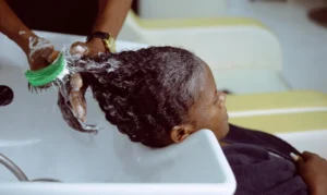 A Black woman receiving a chemical hair treatment in a salon basin, representing the potential chemical exposure linked to uterine and ovarian cancer claims in hair relaxer lawsuits.