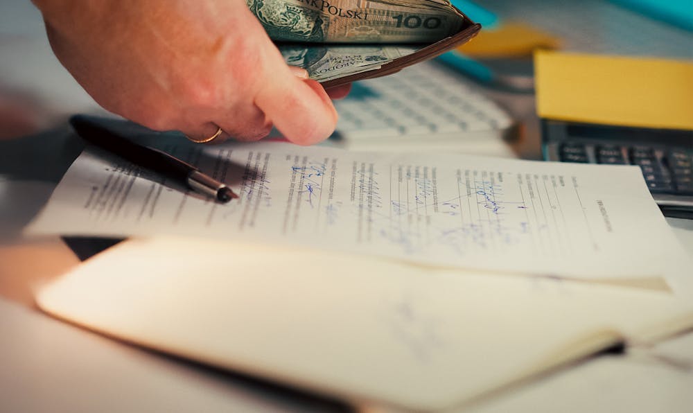 Alt Text: A person checking their wallet for cash over signed legal paperwork and a calculator, representing the financial stress of learning how to file for bankruptcy without a lawyer.