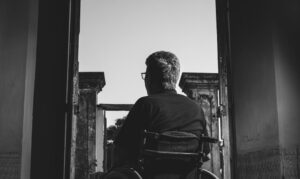 A black and white silhouette of a person in a wheelchair looking through an open doorway, symbolizing a veteran navigating the complex VA disability claims and appeals process.