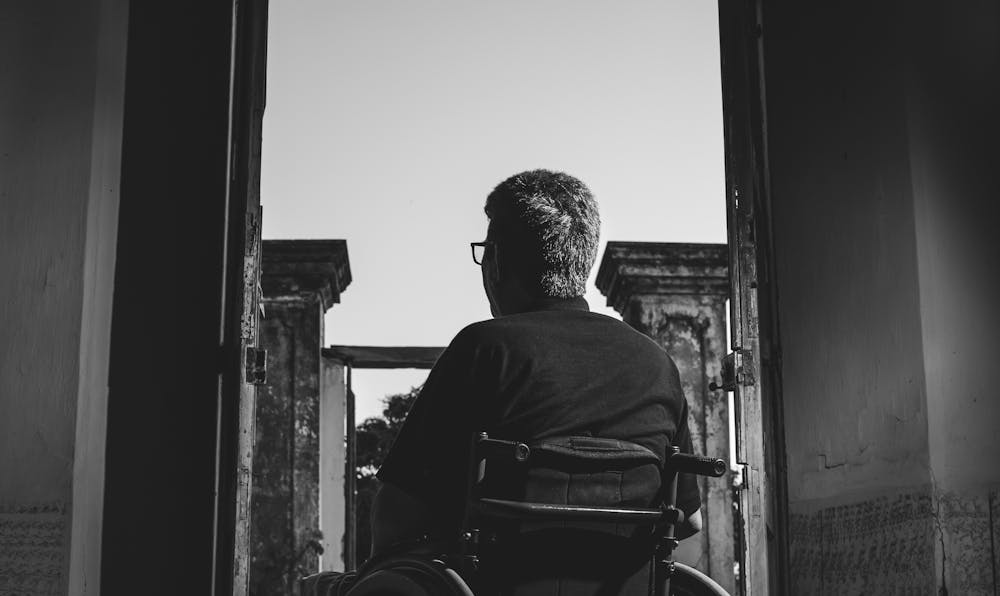 A black and white silhouette of a person in a wheelchair looking through an open doorway, symbolizing a veteran navigating the complex VA disability claims and appeals process.