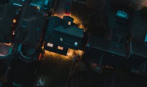 Aerial view of a neighborhood during a blackout, showing one brightly lit home powered by a whole house generator surrounded by dark houses.