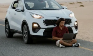 Young man using a laptop next to a white SUV on a desert road.