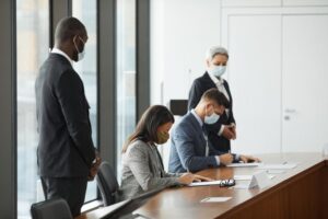 "Diverse group of professionals wearing business attire and protective face masks while signing legal documents at a conference table."