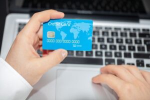 "A person holding a blue credit card featuring a world map design over a laptop keyboard, symbolizing online shopping and credit card options."