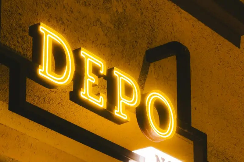 A bright yellow neon sign displaying the word "DEPO" against a textured wall, representing the Depo-Provera contraceptive injection currently at the center of nationwide product liability litigation.