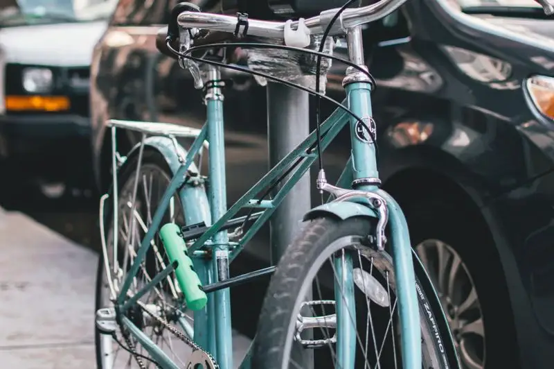 A vintage light blue bicycle locked to a post on a city street, demonstrating bike security which is often covered by renters insurance.