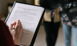 Alt Text: A person holding a pen and a clipboard with a legal document, representing the process of reviewing an estate planning basics checklist to organize family assets.