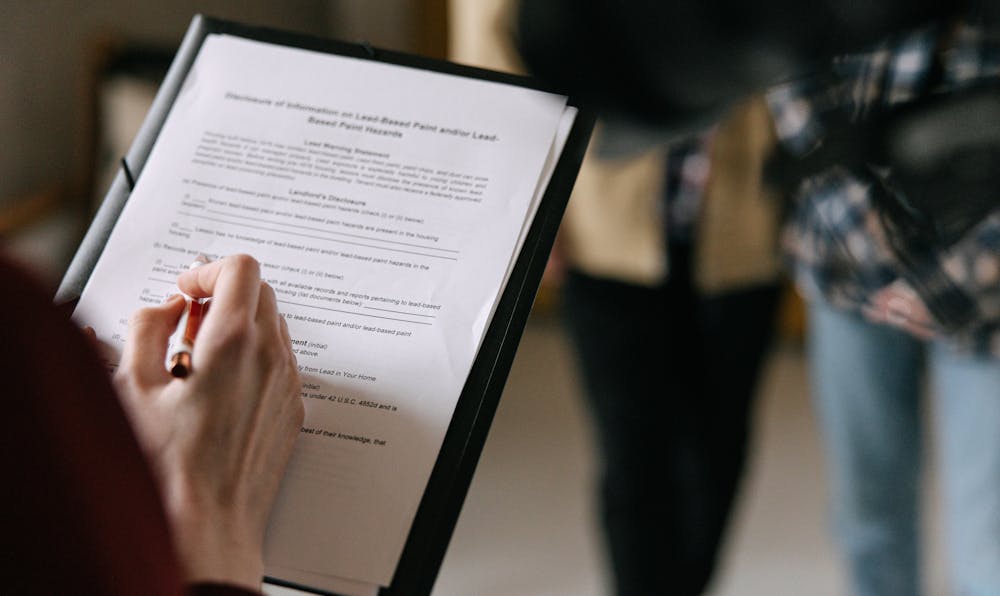 Alt Text: A person holding a pen and a clipboard with a legal document, representing the process of reviewing an estate planning basics checklist to organize family assets.