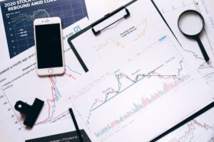 Top-down view of an office desk with stock market charts showing technical analysis patterns, an S&P 500 performance graph, a smartphone, and a magnifying glass.