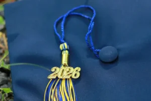 A close-up of a dark blue graduation cap featuring a blue and gold tassel with a metallic gold "2026" year charm resting on top.