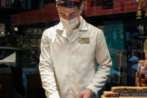 A food service worker in a white uniform preparing pastries behind a glass counter, illustrating the types of customarily tipped occupations that may qualify for the new federal tax deductions.