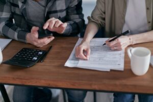 "A couple sitting at a wooden desk filling out financial tax forms with a calculator, pen, and smartphone, illustrating 2026 tax deductions and filing updates."