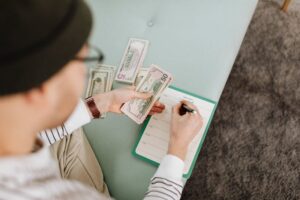 Person holding cash and writing on a notepad, illustrating the careful budgeting and withdrawal planning needed to make your money last. (Retirement Income Planning Make Your Savings Last