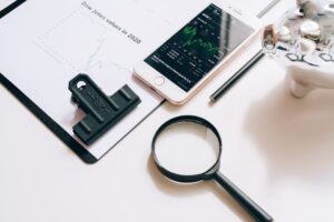 "A magnifying glass, a smartphone displaying stock market trends, a silver piggy bank, and investment charts on a desk, representing the financial research process for a Vanguard 2040 Fund (VFORX) review."