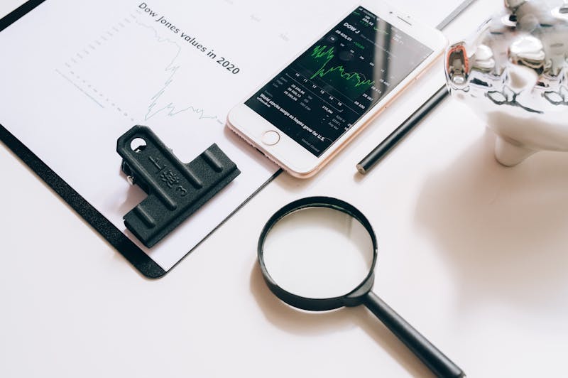 "A magnifying glass, a smartphone displaying stock market trends, a silver piggy bank, and investment charts on a desk, representing the financial research process for a Vanguard 2040 Fund (VFORX) review."