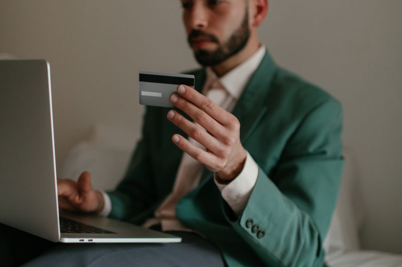 "A businessman in a green suit holding a credit card while using a laptop to manage company finances."