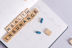 "Wooden tiles spelling 'HEALTH INSURANCE' on a white calendar with two blue pills, illustrating health insurance planning and the 2026 ACA subsidy changes."