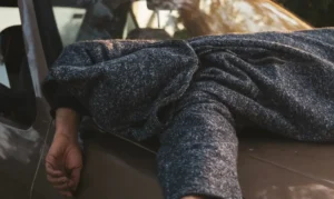 A distressed person slumped over the hood of a car, representing the stressful aftermath of a DUI conviction and the search for high-risk car insurance.