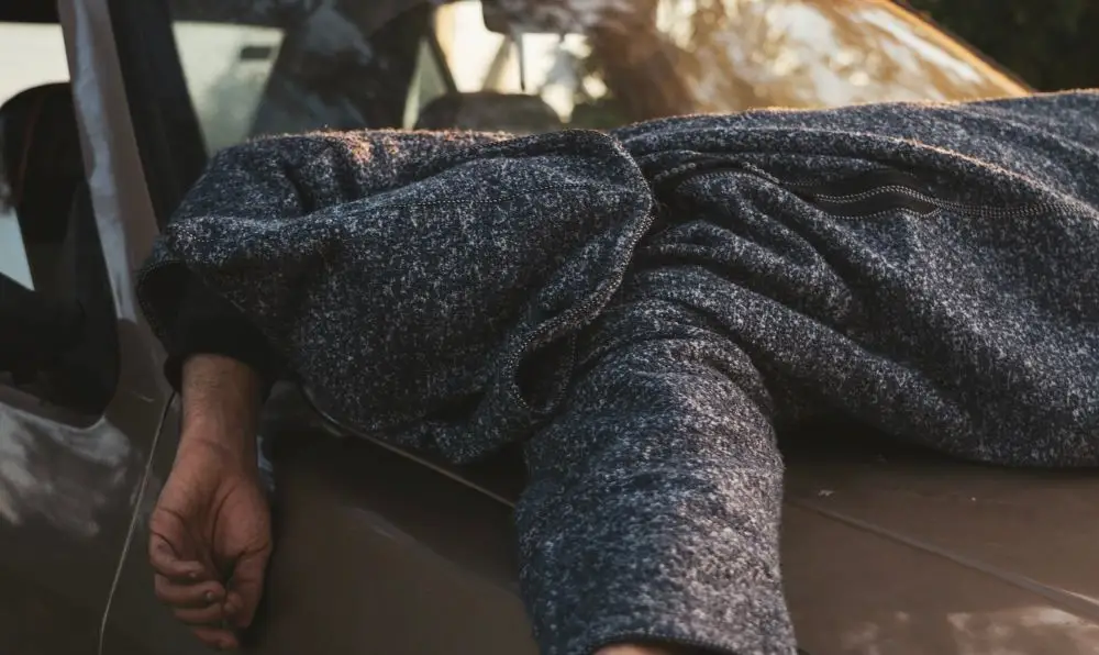 A distressed person slumped over the hood of a car, representing the stressful aftermath of a DUI conviction and the search for high-risk car insurance.