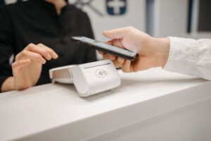 "A patient paying a medical bill with a smartphone at a hospital front desk, illustrating how healthcare expenses affect credit scores under 2026 rules."