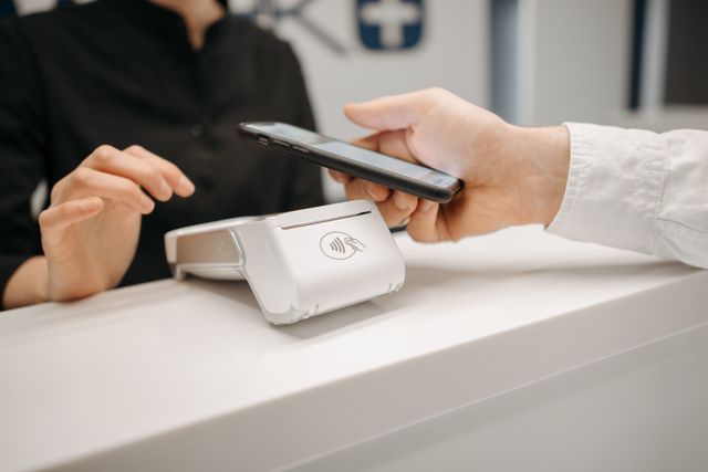 "A patient paying a medical bill with a smartphone at a hospital front desk, illustrating how healthcare expenses affect credit scores under 2026 rules."
