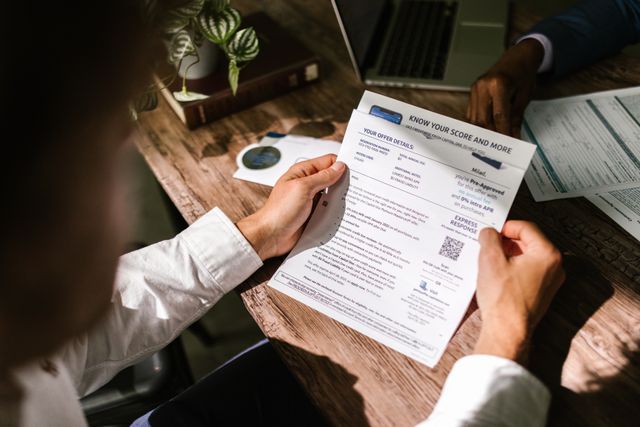 "A person reviewing a pre-approved financial document and credit score summary on a wooden desk next to a laptop."