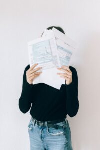 A stressed woman covering her face with complicated paperwork and documents, illustrating the confusion and stress of choosing between full coverage and liability car insurance.