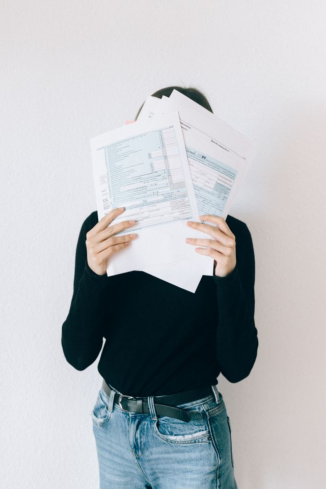A stressed woman covering her face with complicated paperwork and documents, illustrating the confusion and stress of choosing between full coverage and liability car insurance.