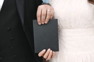 "A bride and groom holding a blank black card, symbolizing the timeline and waiting period for a marriage green card application."