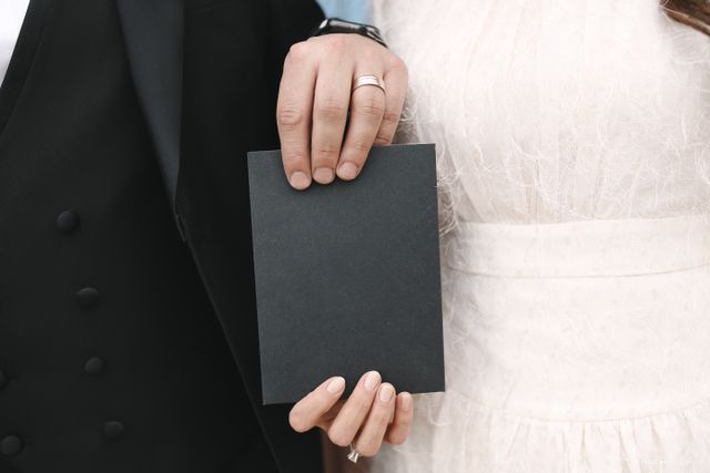 "A bride and groom holding a blank black card, symbolizing the timeline and waiting period for a marriage green card application."