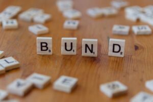 "Scrabble tiles spelling out the word 'BUND' on a wooden table, representing German government bonds as a key fixed-income investment for beginners."