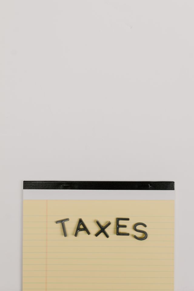 "A yellow lined legal notepad with the word 'TAXES' spelled out in dark, block letters on a plain white background."