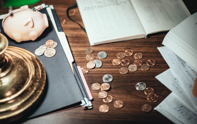 A piggy bank, scattered coins, and an open notebook on a wooden desk, symbolizing healthcare budgeting and saving with HSA or FSA accounts.