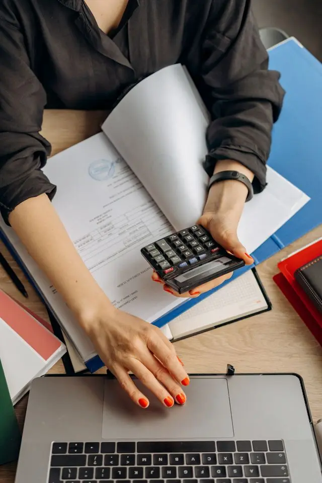 An accountant or freelancer reviewing financial documents, holding a calculator, and typing on a laptop to manage health insurance costs and budget plan without a job.