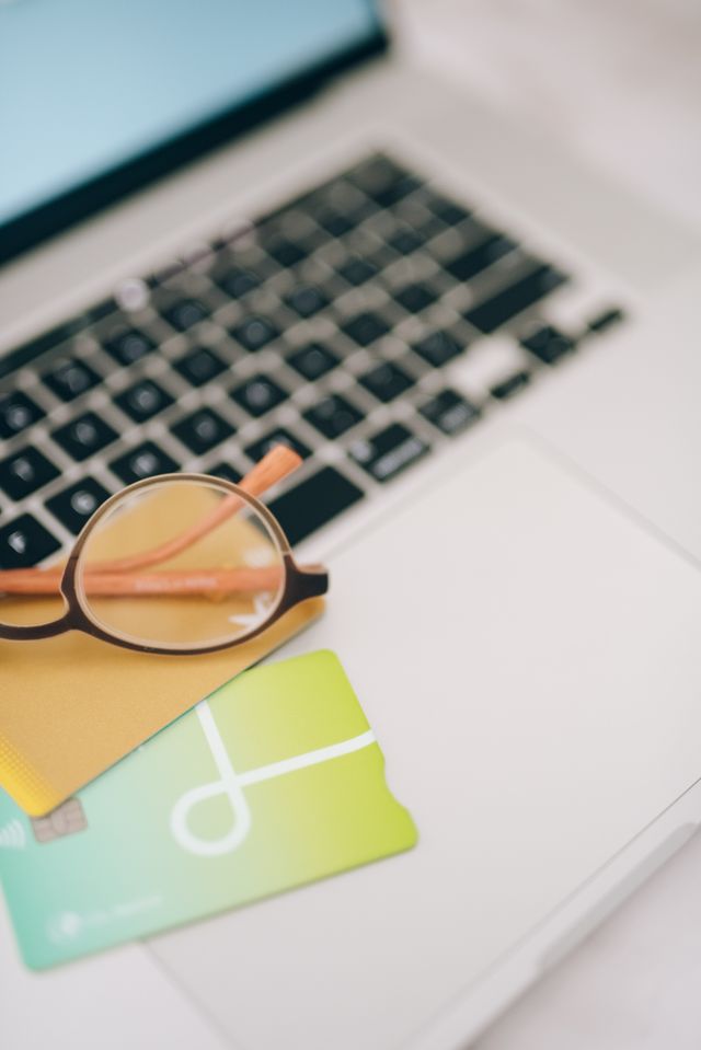 A credit card with a chip and contactless payment symbol sitting on a laptop next to a pair of eyeglasses.