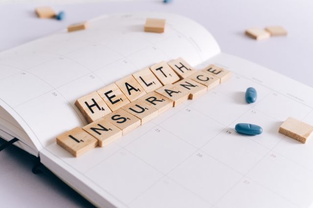A desk calendar displaying word tiles spelling out 'HEALTH INSURANCE' next to a few blue pills, capturing the process of filing a health insurance appeal for a denied claim