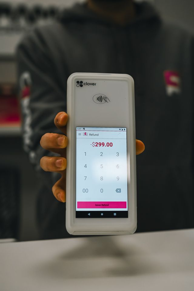 A person holding a Clover Flex POS terminal displaying a pending refund of $299.00 on the screen, illustrating how to get bank fees or overdraft charges refunded.