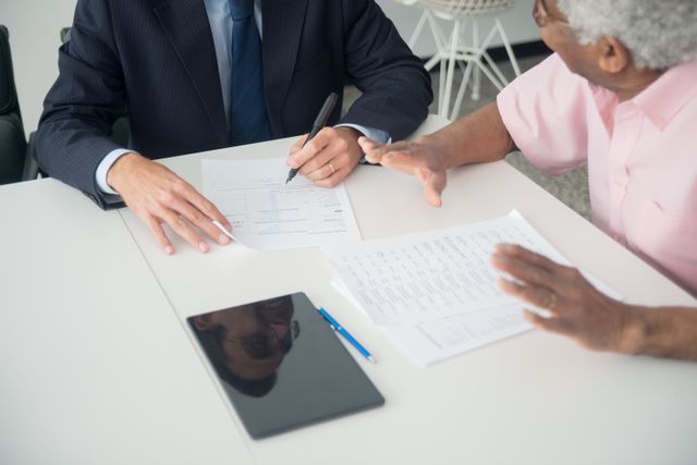 A close-up shot of a financial advisor in a suit filling out life insurance paperwork with an elderly male client during a consultation meeting.