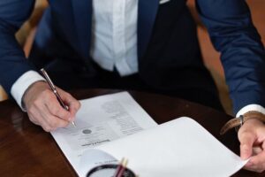 A person in a business suit signing a legal document on a wooden table, representing the authorization and execution of a Power of Attorney.