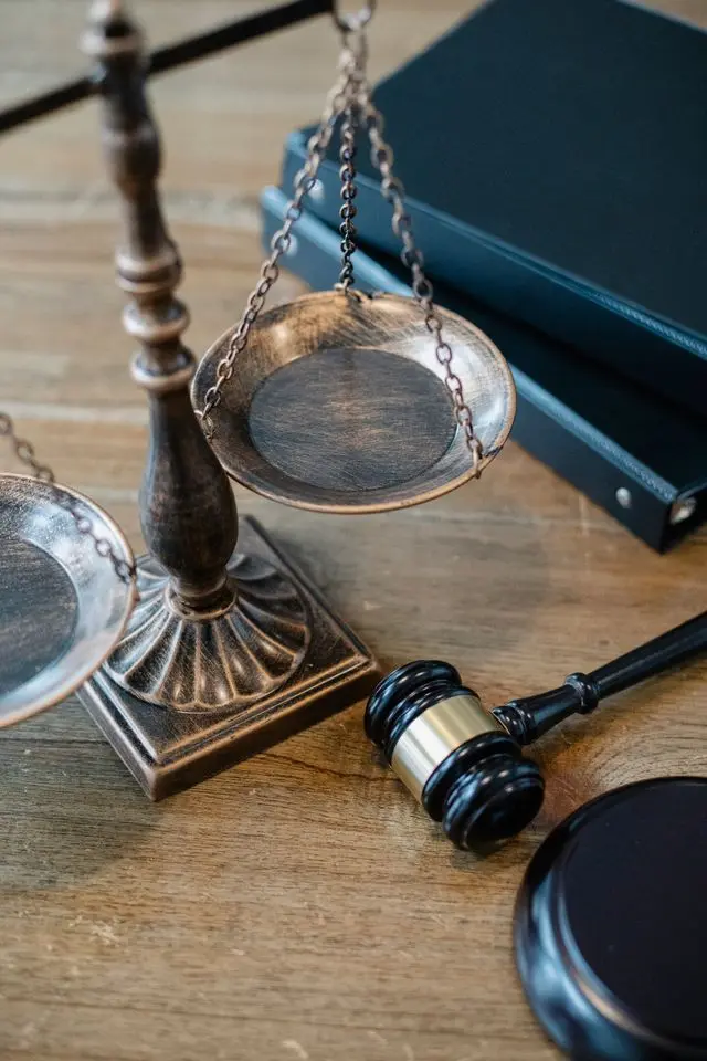 A wooden justice scale, a judge's gavel, and legal law books on a wooden desk.