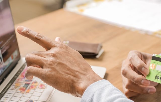 A close-up of a person pointing at a laptop screen while holding a credit card, illustrating the process of online shopping, electronic payments, or reviewing unauthorized credit card transactions.